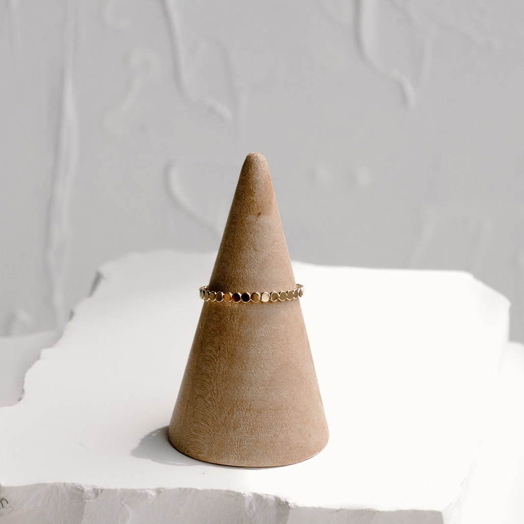 Minimal dot stacking ring in 14k gold filled and sterling silver, displayed on neutral ring cone with textured white backdrop